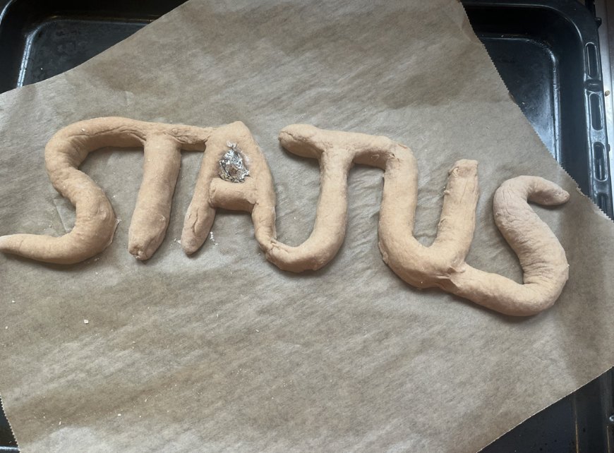 raw dough shaped into the word STATUS on baking paper, with a piece of tin foil in the A