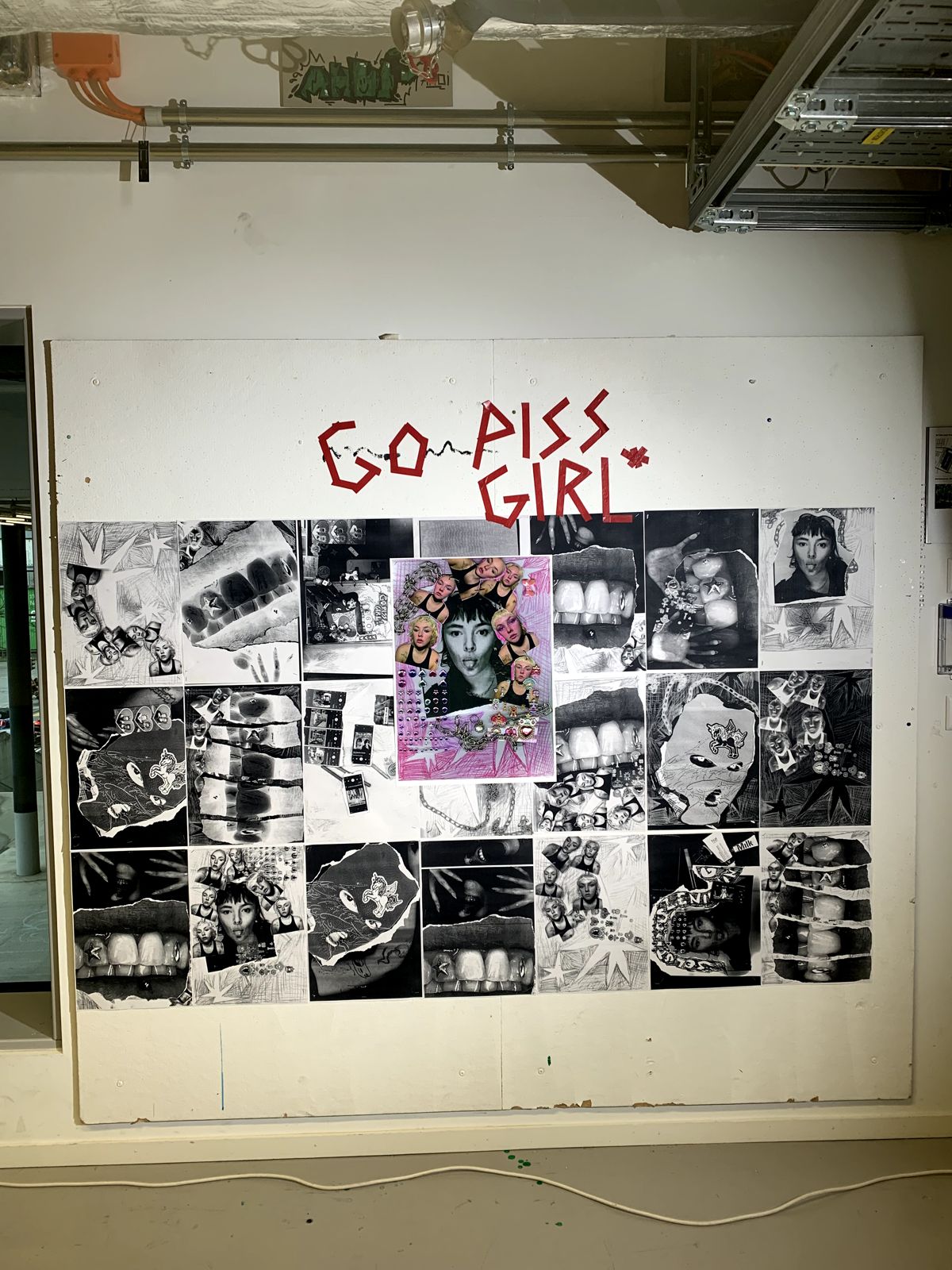 poster wall in an exhibition: black and white collage posters in a grid around a pink cover poster, the words GO PISS GIRL written above in red tape