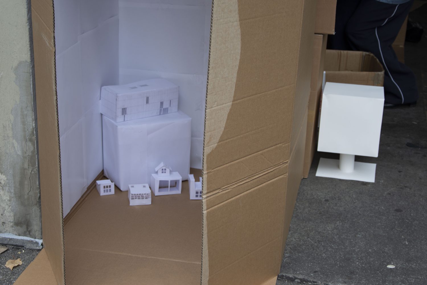 inside the box: white paper walls, a large paper building on a plinth resembling the Kunsthaus extension, and small, different paper houses in front of it