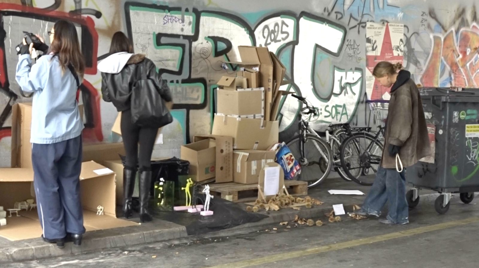 visitors looking at the works of the street exhibition in the underpass, among cardboard boxes and graffiti