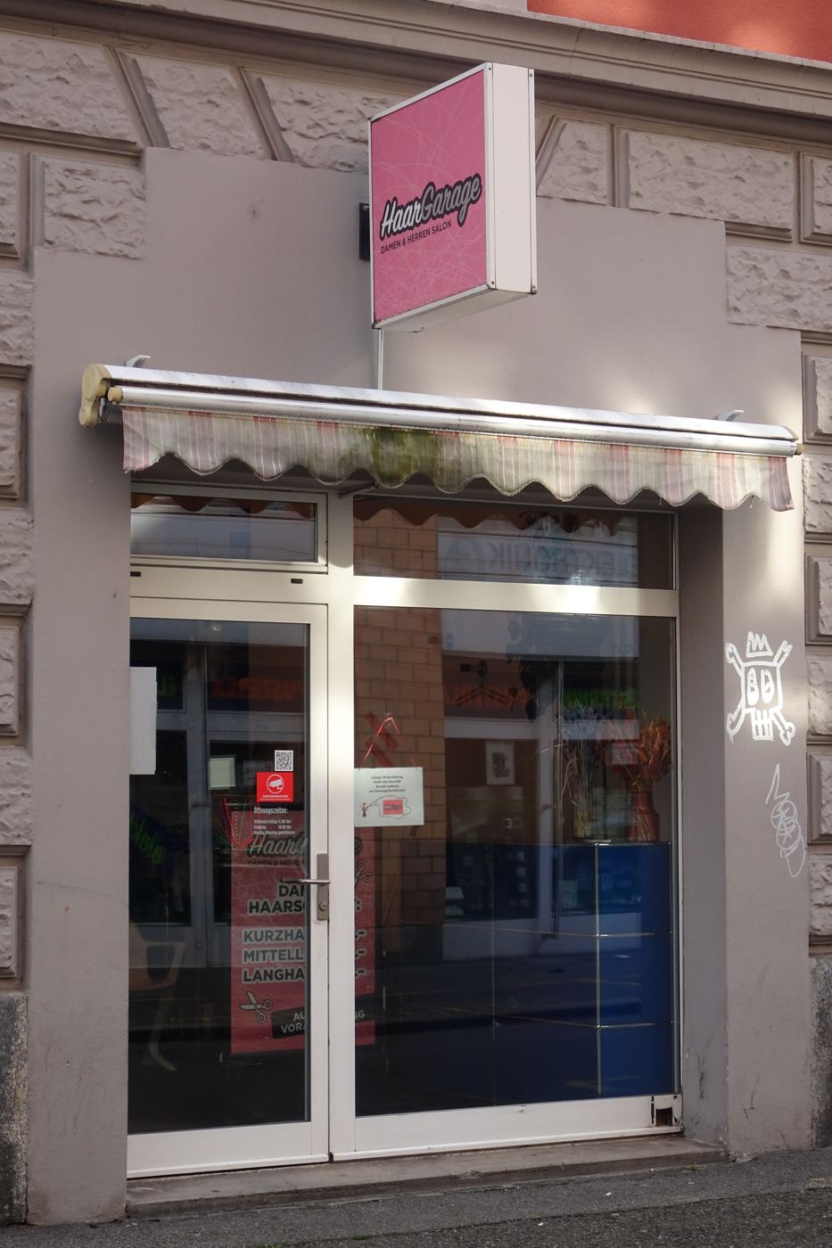 HaarGarage, pink light box sign over a faded awning